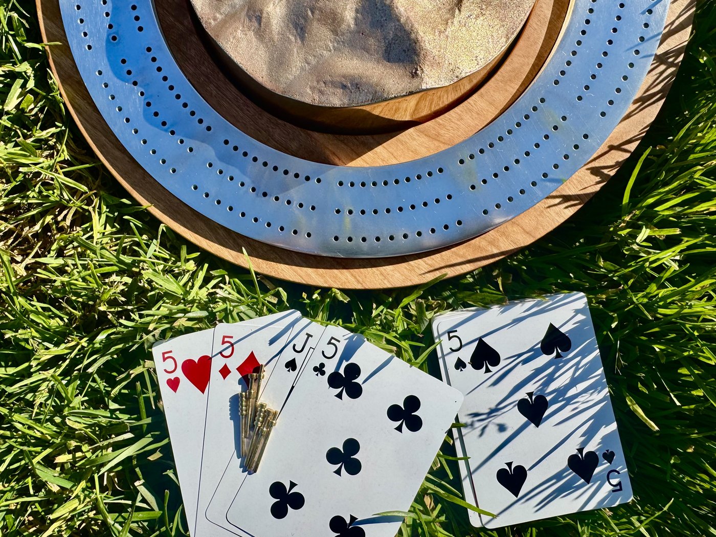 The Crib cribbage board with cards and pegs resting in grass